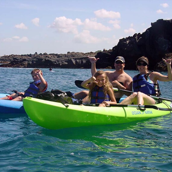 A family of paddles a kayak, smiling and enjoying their time together on a clam lake.