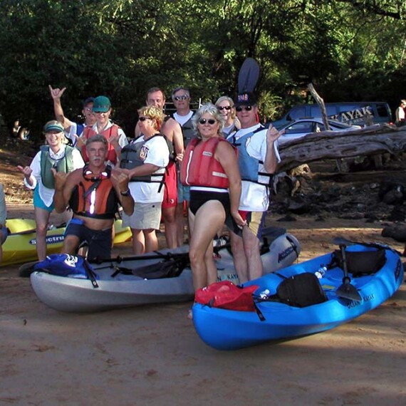 A cheerful group of people stands in front of their kayaks, capturing a moment of camaraderie by water.