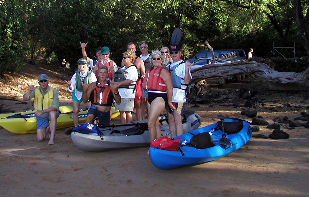 A cheerful group of people stands in front of their kayaks, capturing a moment of camaraderie by water.