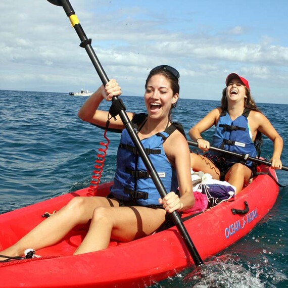 Two woman enjoying a kayaking adventure on Wailea ocean, surrounded by clam waters and a bright sky.