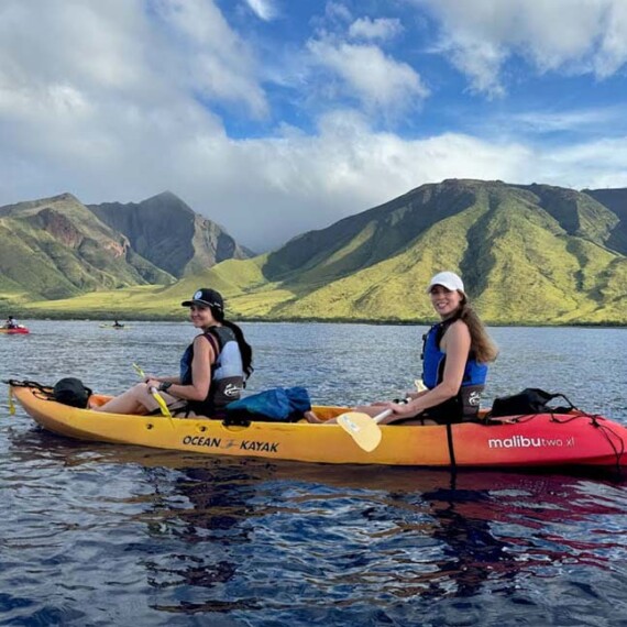 Two people in a kayak on the ocean, with impressive mountains providing a picturesque backdrop.