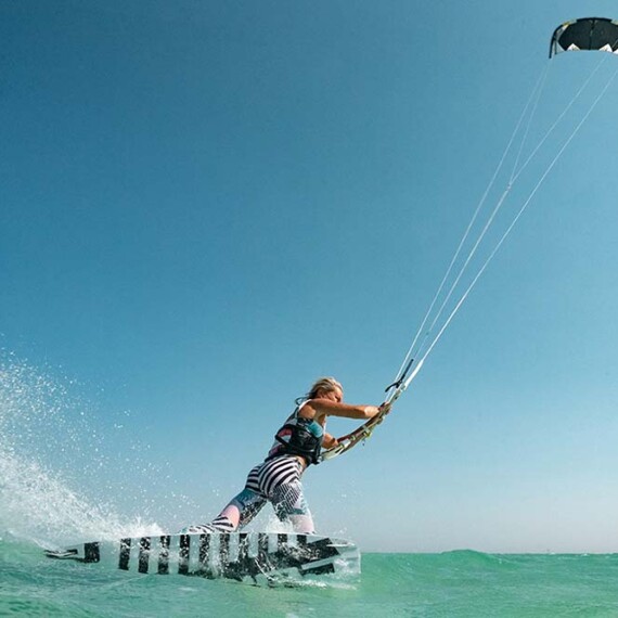 A lady kiteboarding on the ocean, skillfully maneuvering with a colorful kite against a clear blue sky.