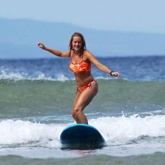 A lady in a bikini skillfully rides a surfboard on waves of ocean, showcasing her surfing prowess.