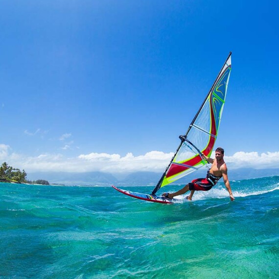 A man is captured windsurfing on the oceans, showcasing his agility as he rides waves under a clear sky.