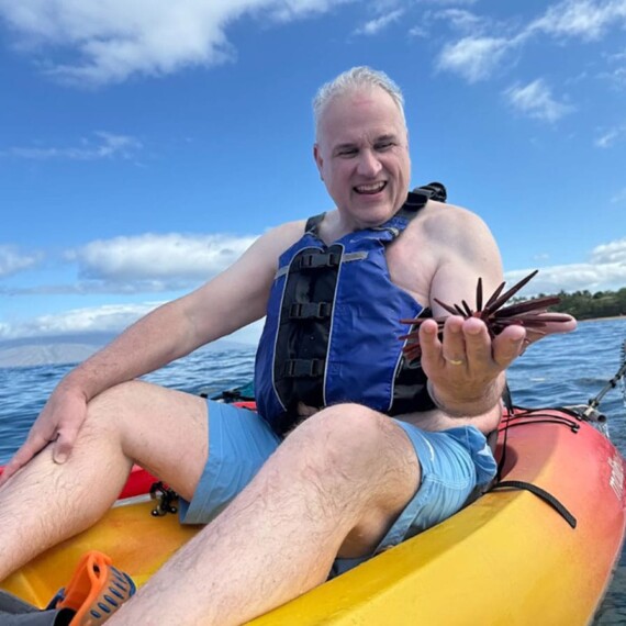 A man in kayak displays a starfish, capturing a quiet movement of ocean exploration and appreciation.