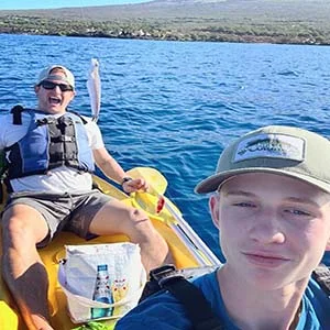 Two men paddling yellow kayaks on serene ocean, surrounded by gentle waves and clear blue skies.