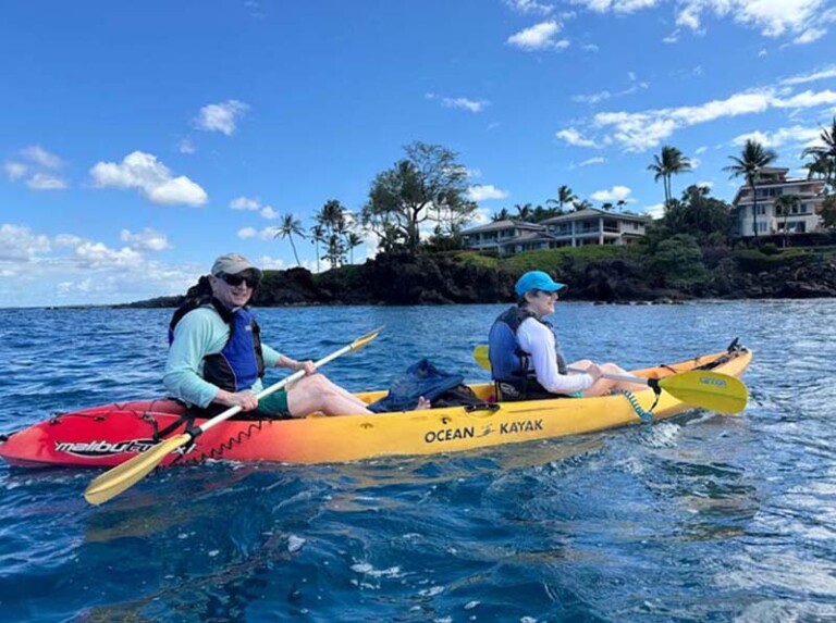 Two people paddling a bright yellow kayak on the calm blue ocean with the South Maui shoreline in the background – Paddle with Dolphins, Kayak Tours in South Maui.