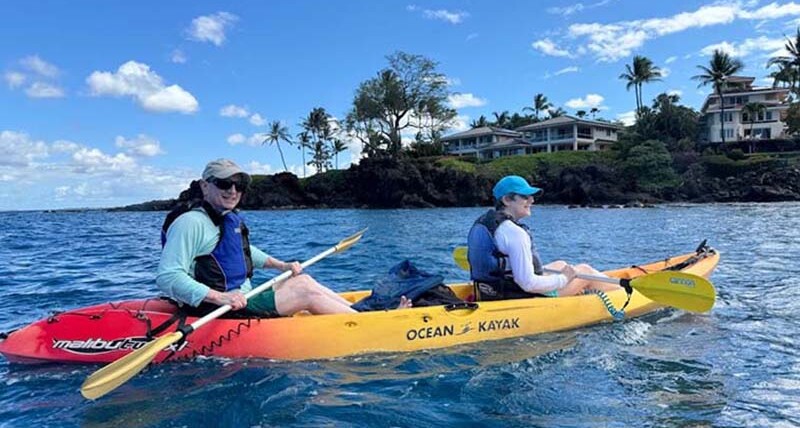Two people paddling a bright yellow kayak on the calm blue ocean with the South Maui shoreline in the background – Paddle with Dolphins, Kayak Tours in South Maui.