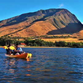 Kayakers wearing life jackets paddling on calm ocean waters in Maui while following Ocean safety guidelines Hawaii near a mountainous coastline.